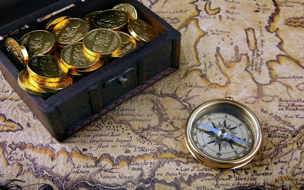 A treasure chest filled with gold coins placed on an antique map alongside a vintage compass