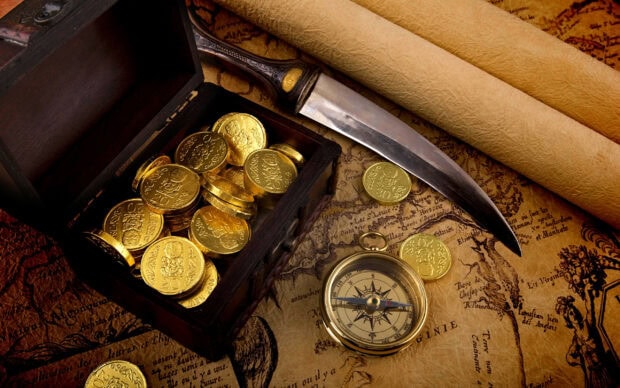 A chest filled with gold coins on an old map surrounded by a compass a sword and a scroll