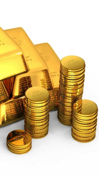 Stacks of shiny gold coins next to gold bars on a white surface