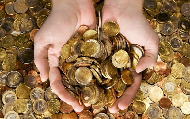 Hands holding a pile of gold coins surrounded by more gold coins on a surface