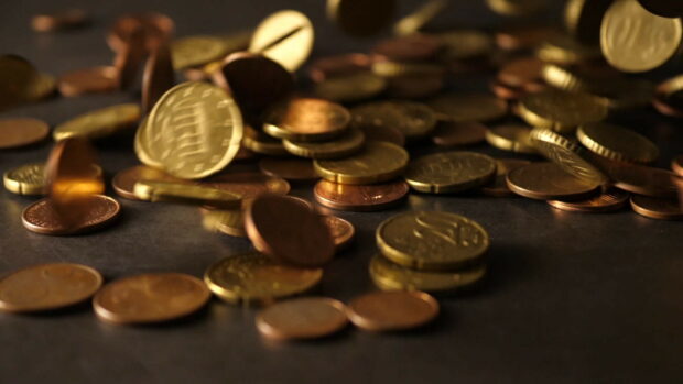 A close up of scattered gold coins on a dark surface showing gold coins