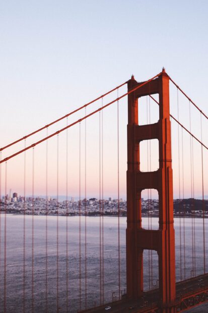 Golden Gate Bridge tower and suspension cables with city skyline in the background at sunset
