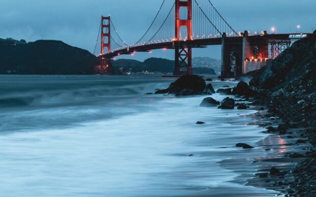 Golden Gate Bridge at dusk with waves crashing on rocky shore