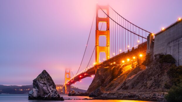 Golden Gate Bridge at dusk with fog and a large rock in the water nearby