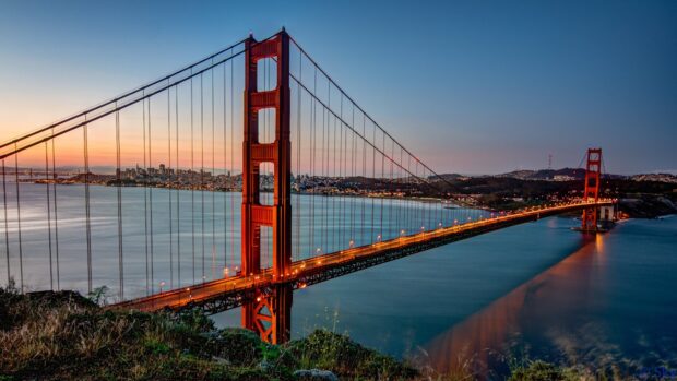 Golden Gate Bridge at sunset over the water with city skyline in the background