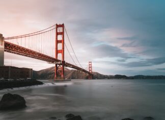 Golden Gate Bridge is seen from the rocky shore with hills in the background at dusk