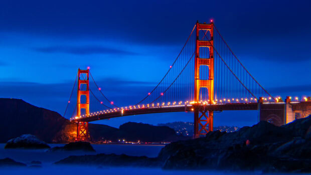 Golden Gate Bridge lit up at night over the bay with dark hills in the background