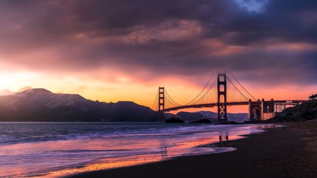 Golden Gate Bridge with mountains at sunset on a calm beach