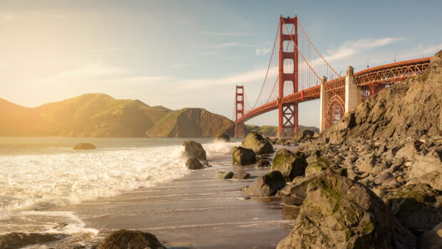 Golden Gate Bridge with rocky beach and waves under clear sky at sunset