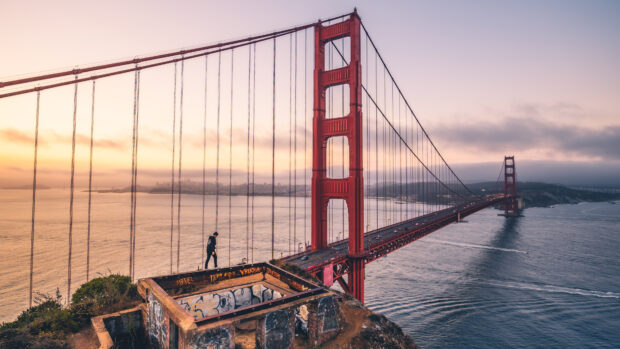 A person walking near the Golden Gate Bridge during sunset in a cityscape view