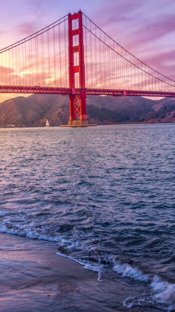 Golden Gate Bridge viewed from the shoreline with waves at sunset in purple sky