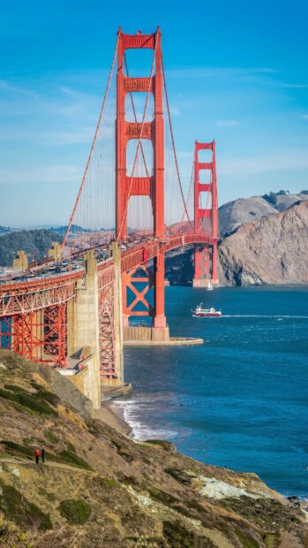 Red Golden Gate Bridge extending over blue water with hills in the background