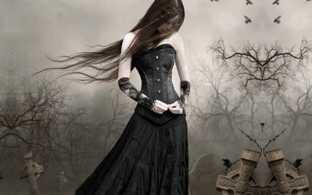 A gothic figure wearing a black corset dress in a dark forest with bare trees and stone crosses