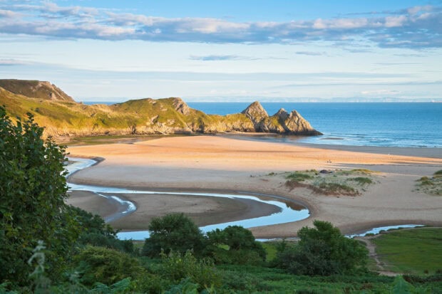 Sandy coastline and rocky hills of Gower Peninsula with winding river and lush greenery