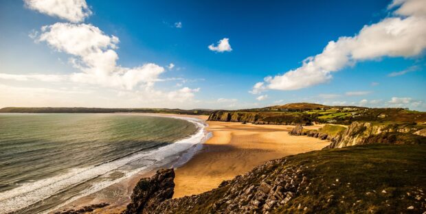 Scenic coastal landscape of Gower Peninsula featuring cliffs and sandy beach on a sunny day
