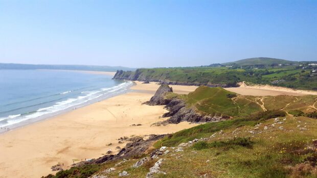 The sandy beach and green cliffs of Gower Peninsula on a clear sunny day