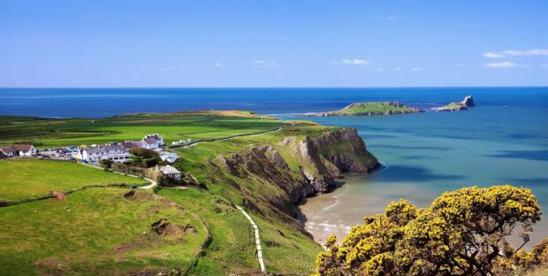 A scenic view of Gower Peninsula cliffs and green fields under a blue sky