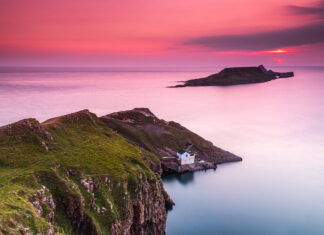 Cliffs and small house on Gower Peninsula at sunset with a pink sky and calm sea