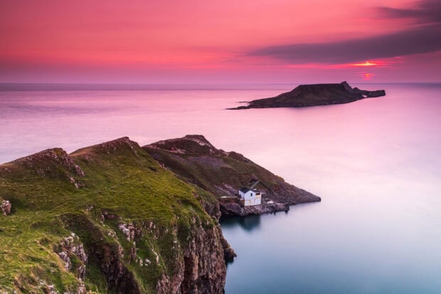 Cliffs and small house on Gower Peninsula at sunset with a pink sky and calm sea
