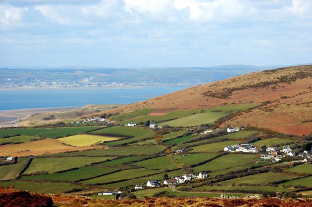 Green fields and hills landscape of Gower Peninsula with small houses and coastline in the distance