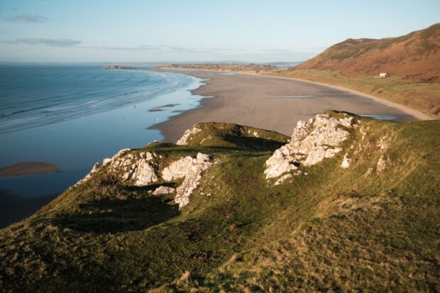 Rocky cliffs and grassy hills overlooking the expansive Gower Peninsula coastline in natural sunlight