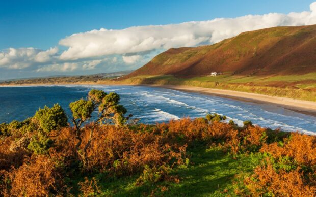 Rolling hills and coastal vegetation on Gower Peninsula with sea waves under a partly cloudy sky