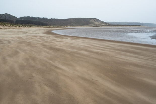 Sandy coastline of Gower Peninsula with hills in the background
