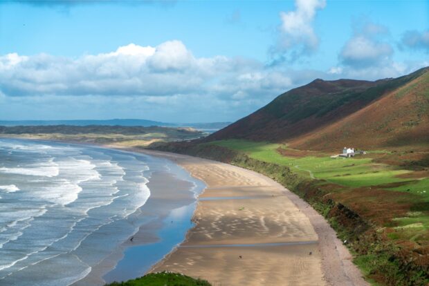 Scenic coastal landscape of the Gower Peninsula with rolling hills and sandy beach under blue sky