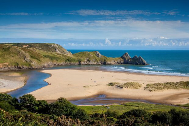 The Gower Peninsula coastline with sandy beach and rocky cliffs under a blue sky