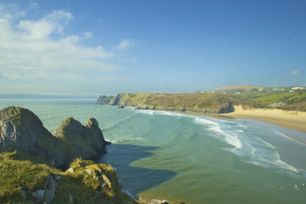 The scenic coastline of Gower Peninsula with cliffs and sandy beach under a bright blue sky