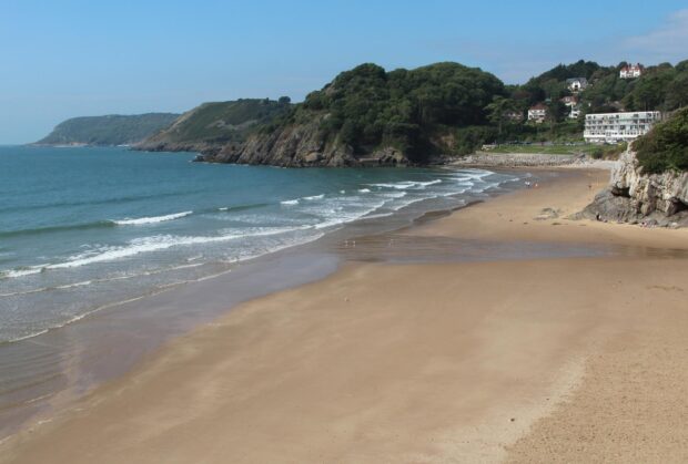 A sandy beach with gentle waves near the green hills of Gower Peninsula