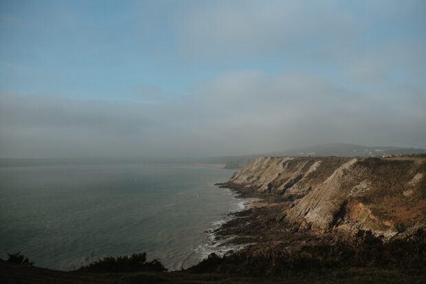 A scenic coastal cliff line along Gower Peninsula under a cloudy sky