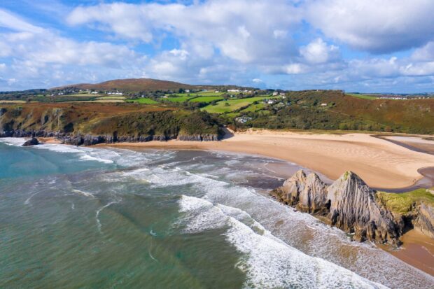 A scenic coastal view of Gower Peninsula with cliffs and green hills under a blue sky