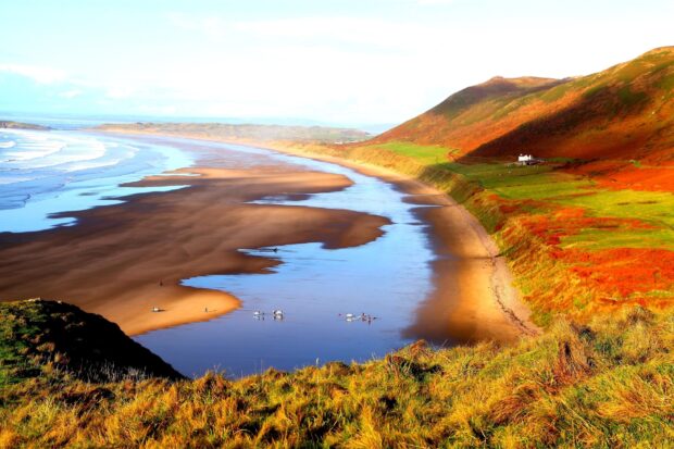 A stunning view of the Gower Peninsula coastline with colorful hills and calm sea waters reflecting the sky