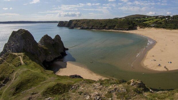 A scenic view of Gower coastline with cliffs sandy beach and green hills