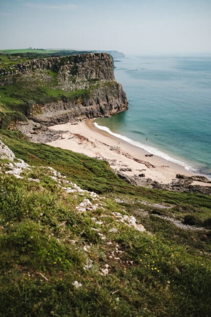 Green cliffs and sandy beach along the Gower Peninsula coastline