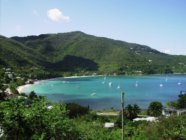 A scenic view of Grenada with green hills and turquoise bay filled with sailboats and lush vegetation