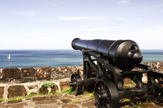 Historic cannon overlooking the ocean in Grenada with a sailing boat in the distance