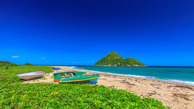 Green boats on the sandy beach with lush vegetation in Grenada