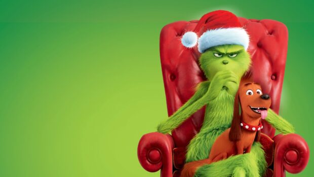 The Grinch wearing a Santa hat sitting on a red chair with a happy brown dog on his lap