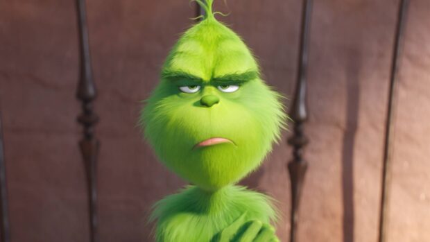 The grinch looking displeased with crossed arms in front of a brown background