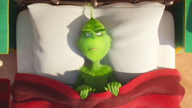 The Grinch lying in bed covered with a red blanket looking thoughtful