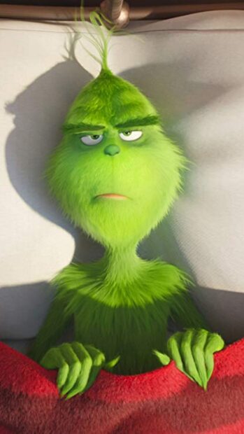 The Grinch looking sleepy while lying in bed with a red blanket covering him