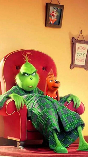 The Grinch sitting on a red armchair wearing a green plaid robe with his dog beside him