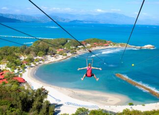 A person enjoying zip lining over a tropical beach with clear blue water in Haiti