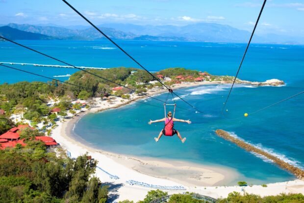 A person enjoying zip lining over a tropical beach with clear blue water in Haiti