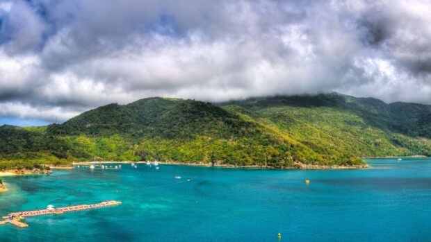Lush green hills of Haiti with turquoise waters and cloudy sky above the landscape