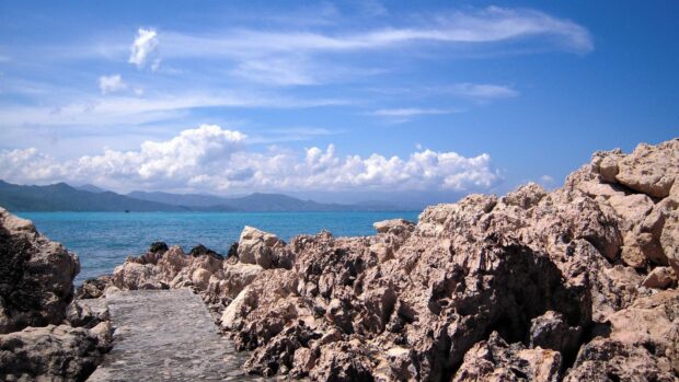 A rocky shore with clear blue sea and distant mountains in Haiti landscape