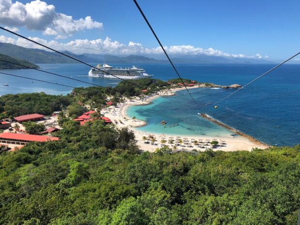 A scenic view of Haiti coastline with a cruise ship docked near the tropical beach and lush green forest