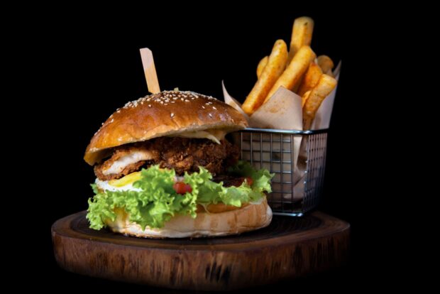 Crispy chicken sandwich with fresh lettuce and tomato served with seasoned fries on a wooden platter